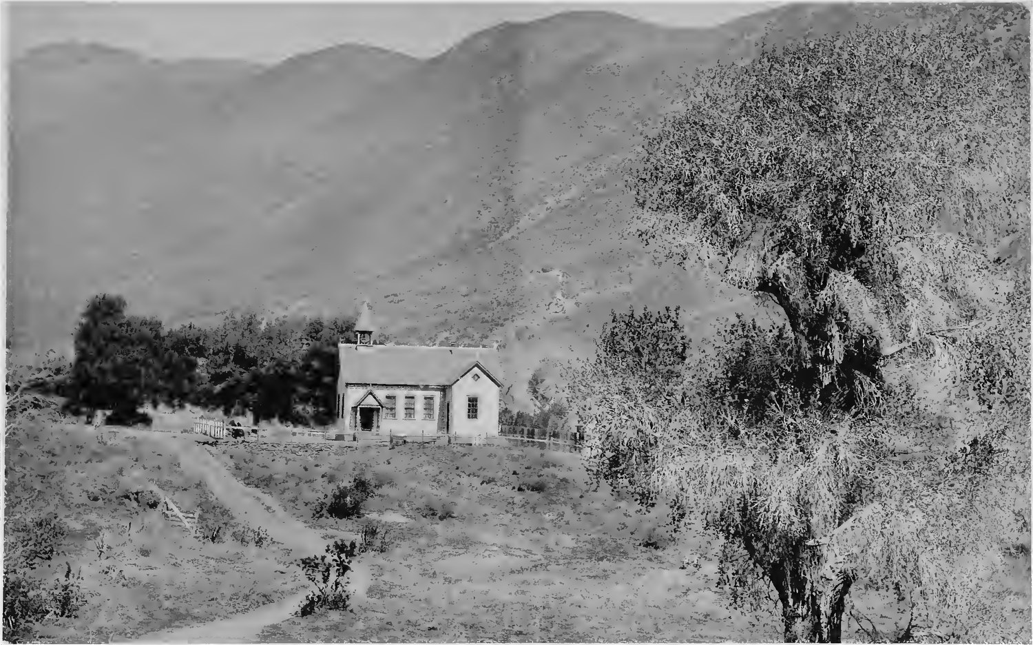 A small white schoolhouse standing alone on a bare hillside below the mountains in the Banner district near Julian, photographed in 1887