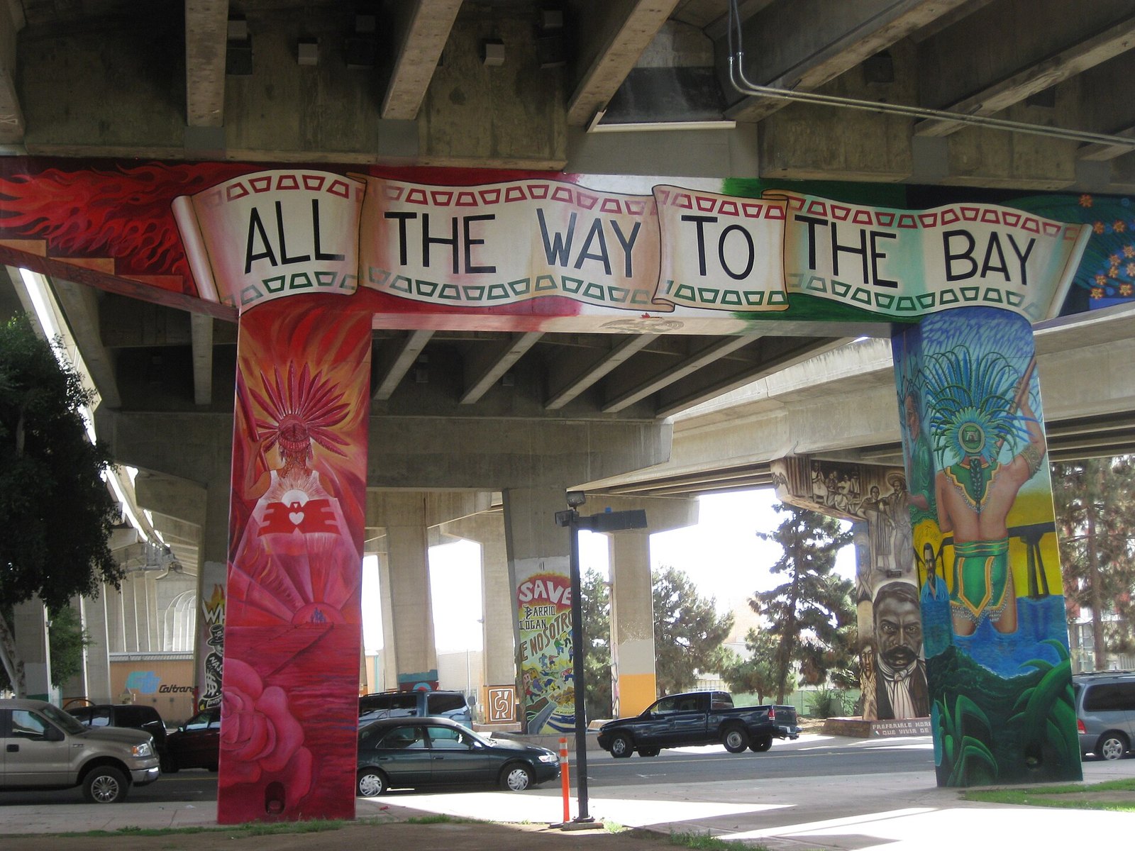 Brightly painted bridge pillars under the freeway, with a banner across them reading All the Way to the Bay