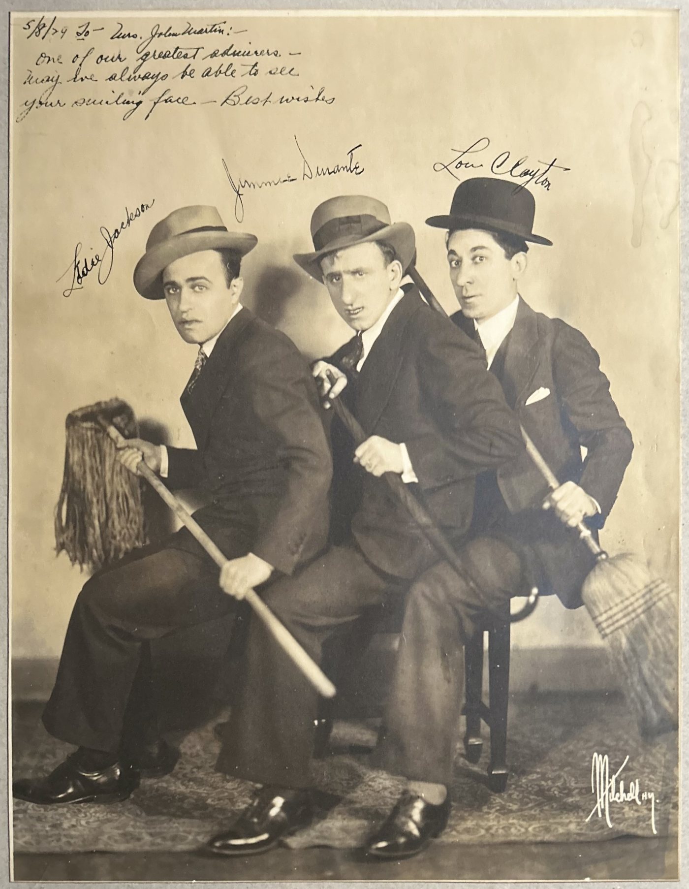 Inscribed 1929 publicity photograph of Eddie Jackson, Jimmy Durante and Lou Clayton seated in a row in hats and suits, holding a mop and a broom