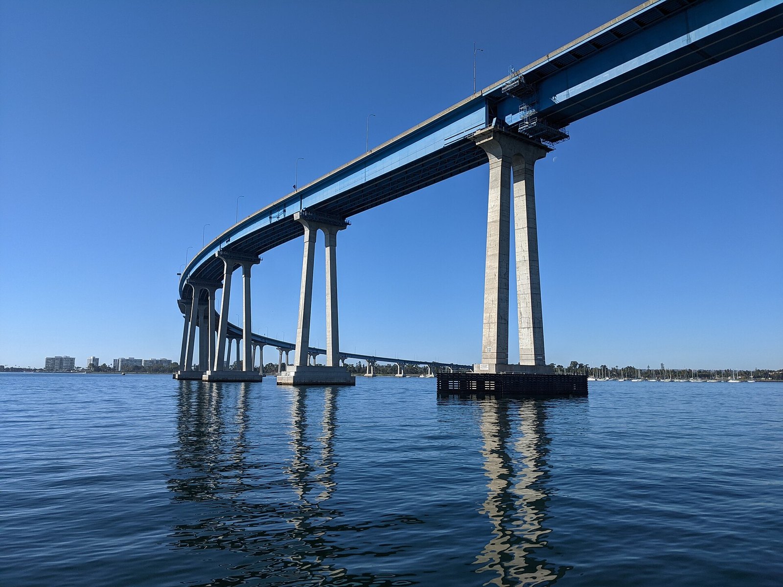 The high curving blue girder bridge on tall concrete piers over calm water