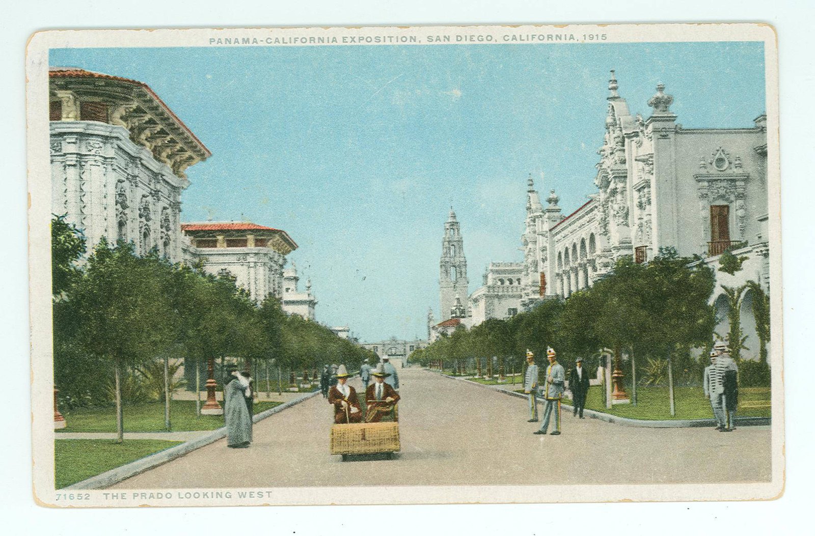 A tinted postcard of a wide tree lined promenade between ornate white Spanish style buildings, with a tower at the far end