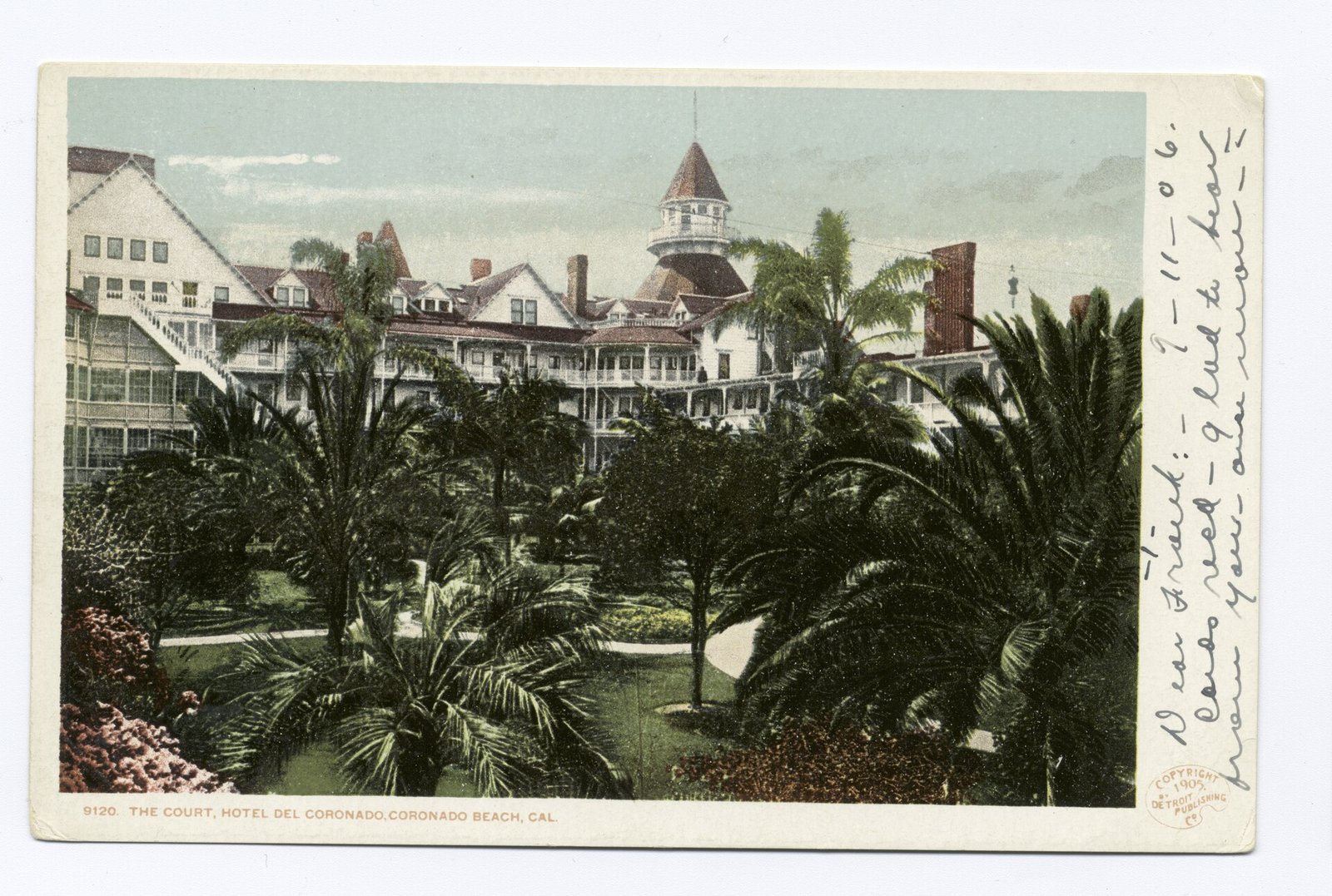 A tinted postcard of a garden courtyard thick with palms and tropical plants, the hotel's white balconied wings and a turret around it, handwriting in the margin