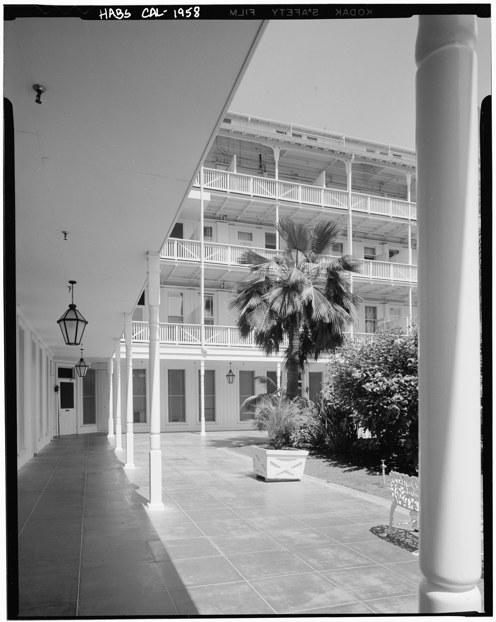A covered walkway with white columns looking onto a courtyard of palms, the hotel's stacked white balconies rising behind