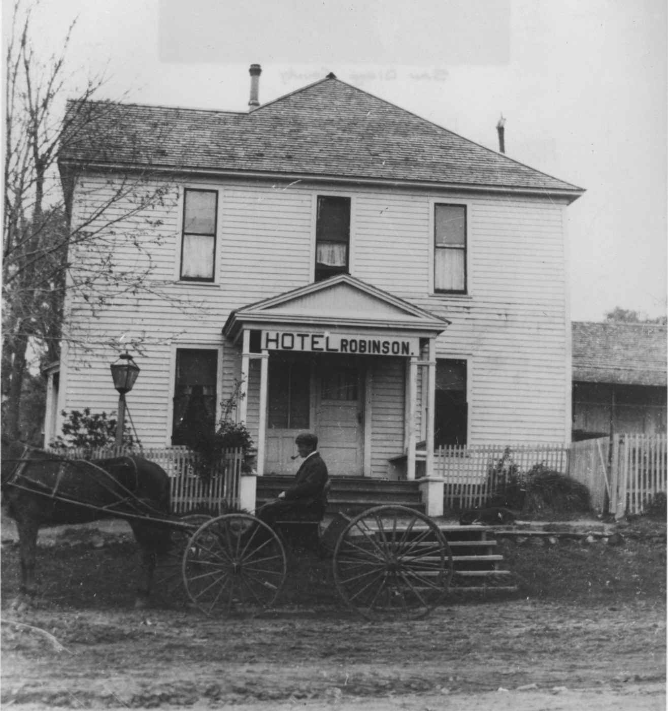 The Hotel Robinson in Julian, California in 1900, a two story frame building with a sign reading Hotel Robinson over the front porch and a man seated in a horse drawn buggy in the road outside