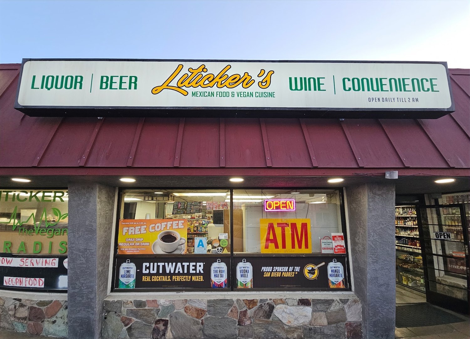A liquor store front under a long white sign reading Liquor, Beer, Liticker's, Mexican Food and Vegan Cuisine, Wine, Convenience, with a red metal awning, a neon open sign and a yellow ATM sign in the window
