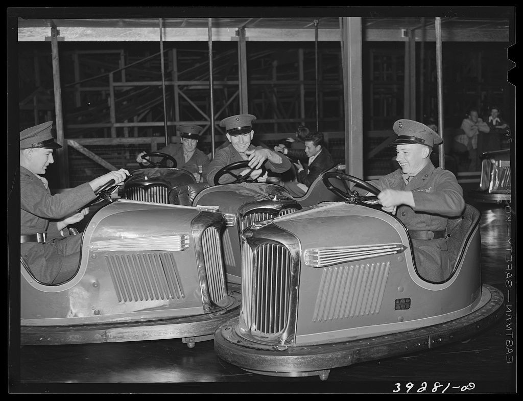 Uniformed Marines in peaked caps laughing as they steer chrome bumper cars on an indoor track