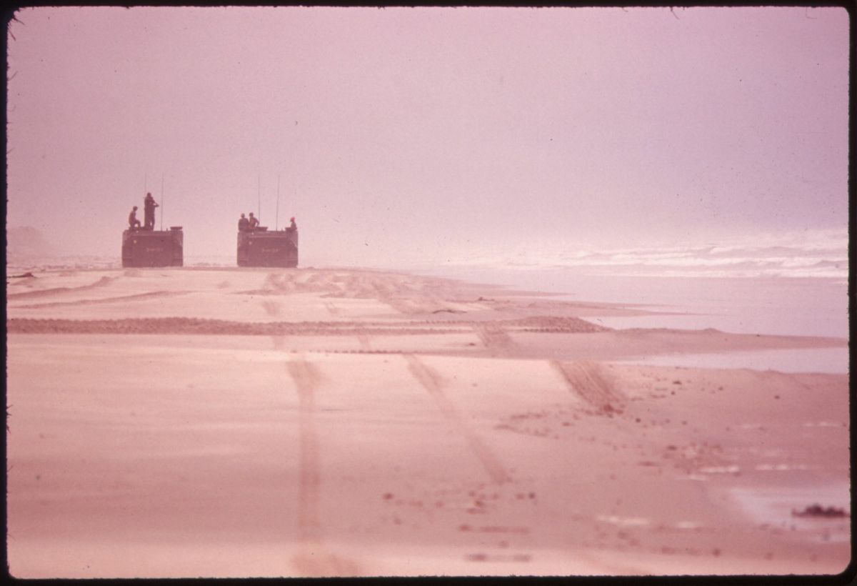 Two amphibious vehicles coming out of the surf onto a long empty beach under a hazy sky
