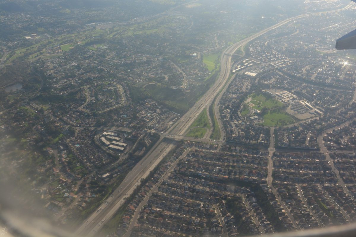An aerial view of a freeway curving through hills and neighborhoods toward a distant bay under a hazy sky