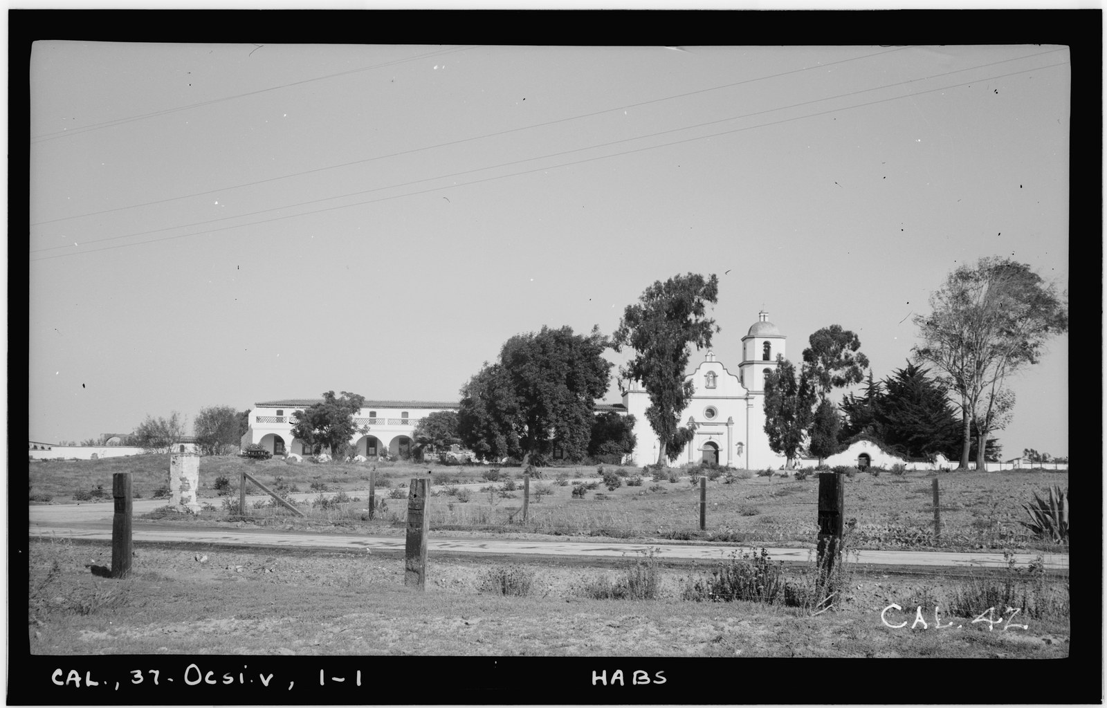 Mission San Luis Rey photographed from across open ground in November 1936, the restored white church and its dome standing among trees