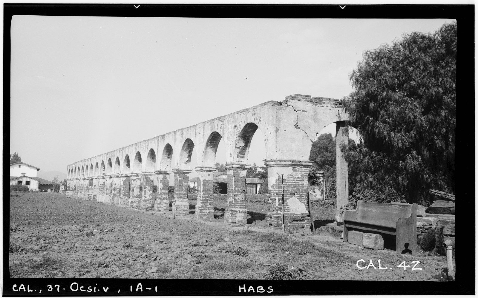 The surviving brick cloister arcade at Mission San Luis Rey in 1936, a long run of arches receding into the distance with a broken pillar in the foreground