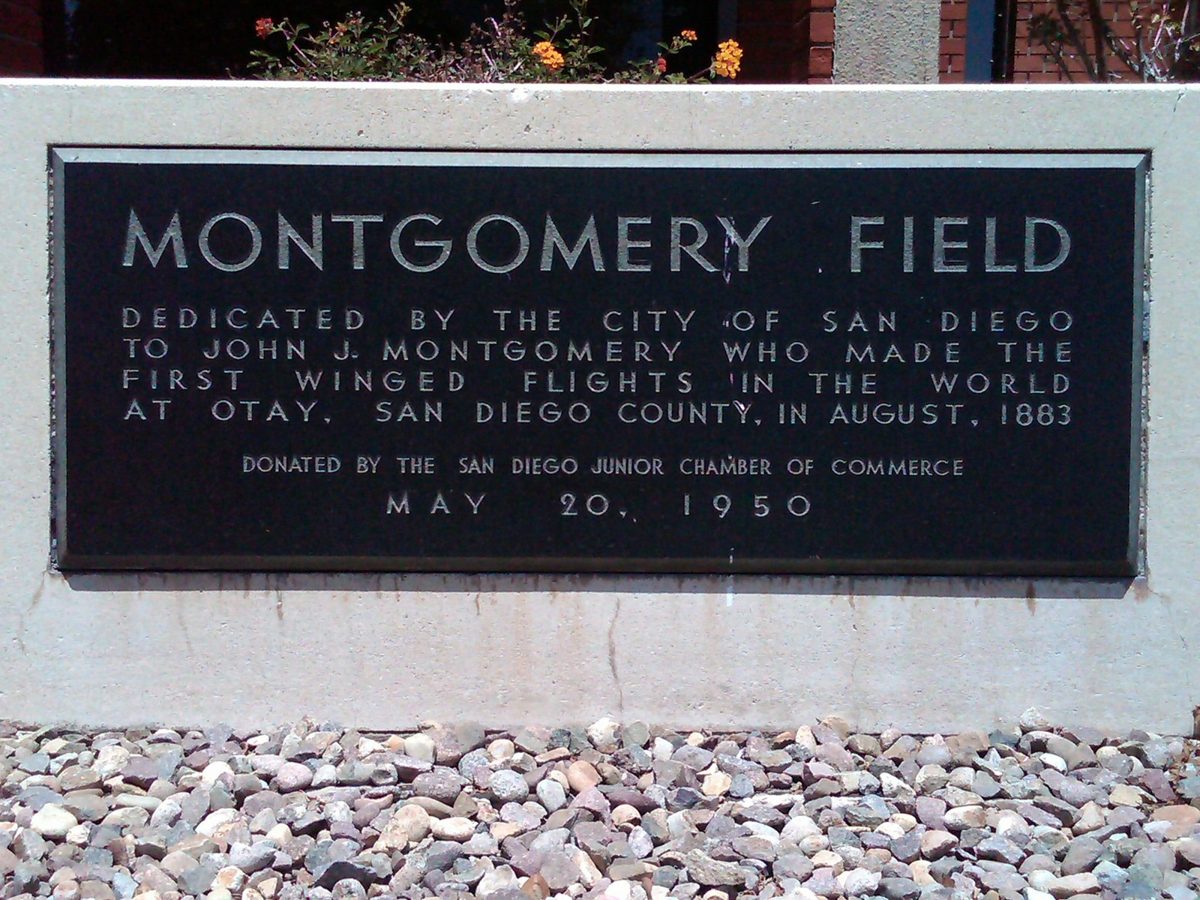 A dark bronze plaque reading Montgomery Field set in a stone base with gravel and flowers around it