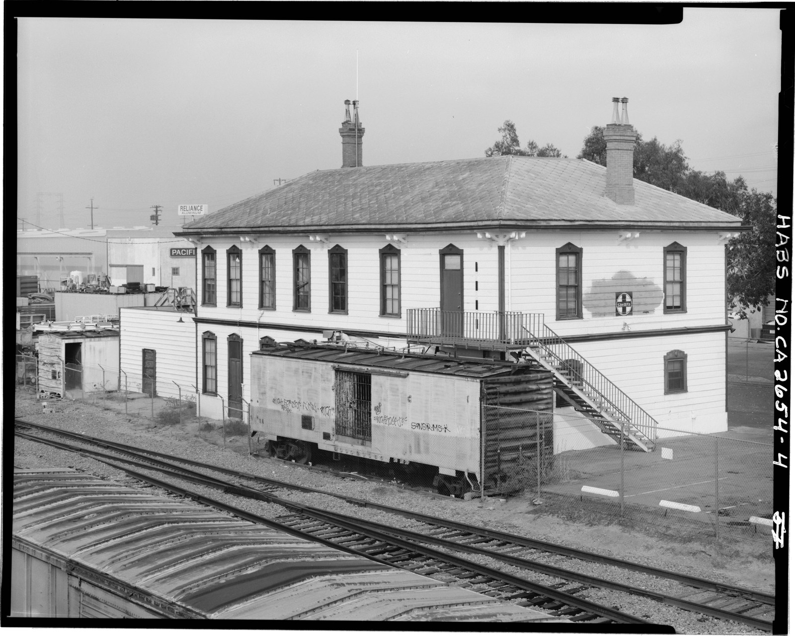 The two story wood National City railroad depot of 1882 seen from across the railroad tracks, with a boxcar standing against its west side