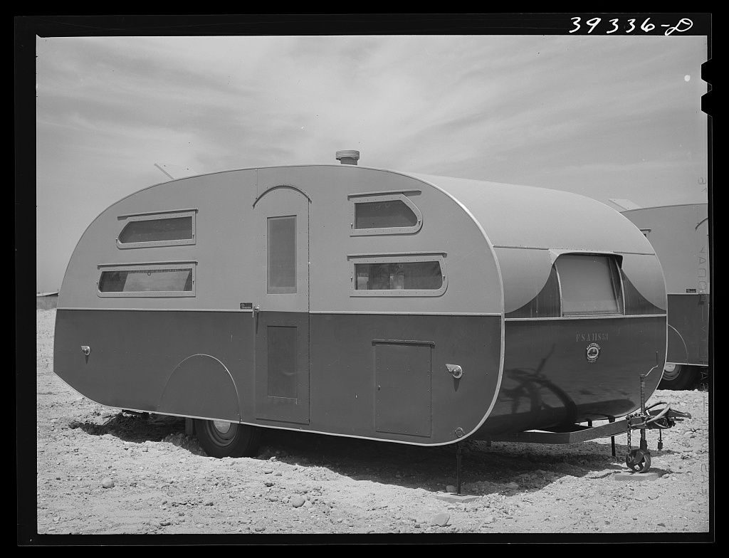 A rounded travel trailer parked on bare dirt under a cloudy sky