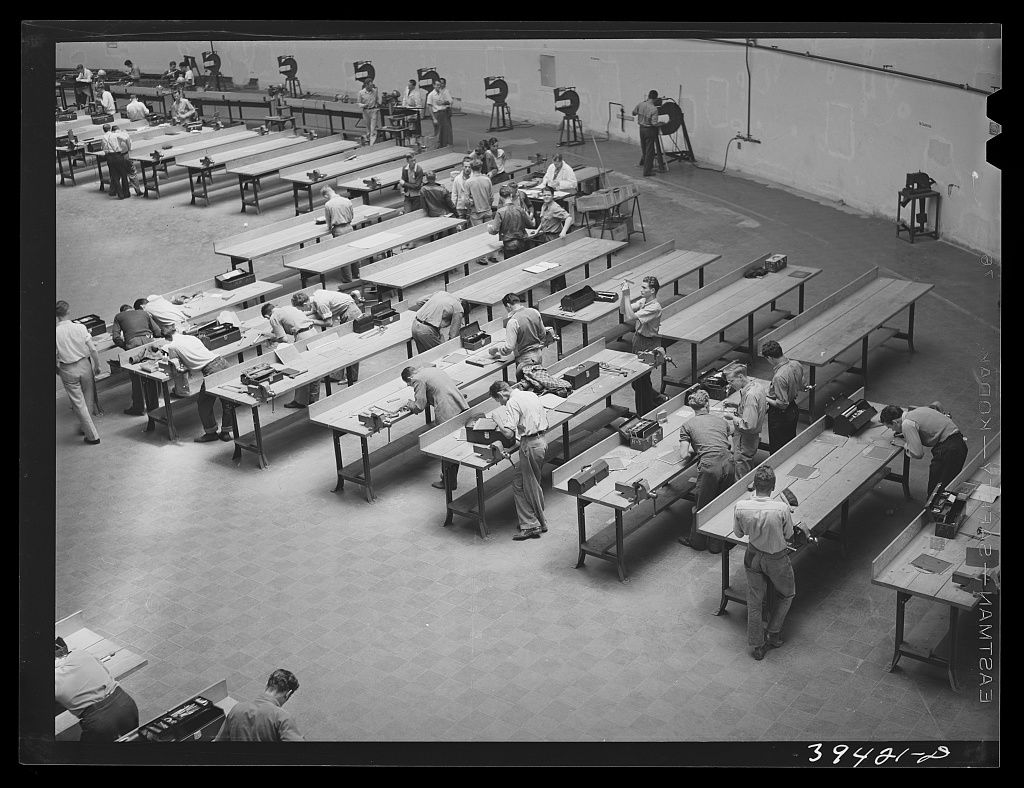 A large workshop of long benches with students working at them, seen from above