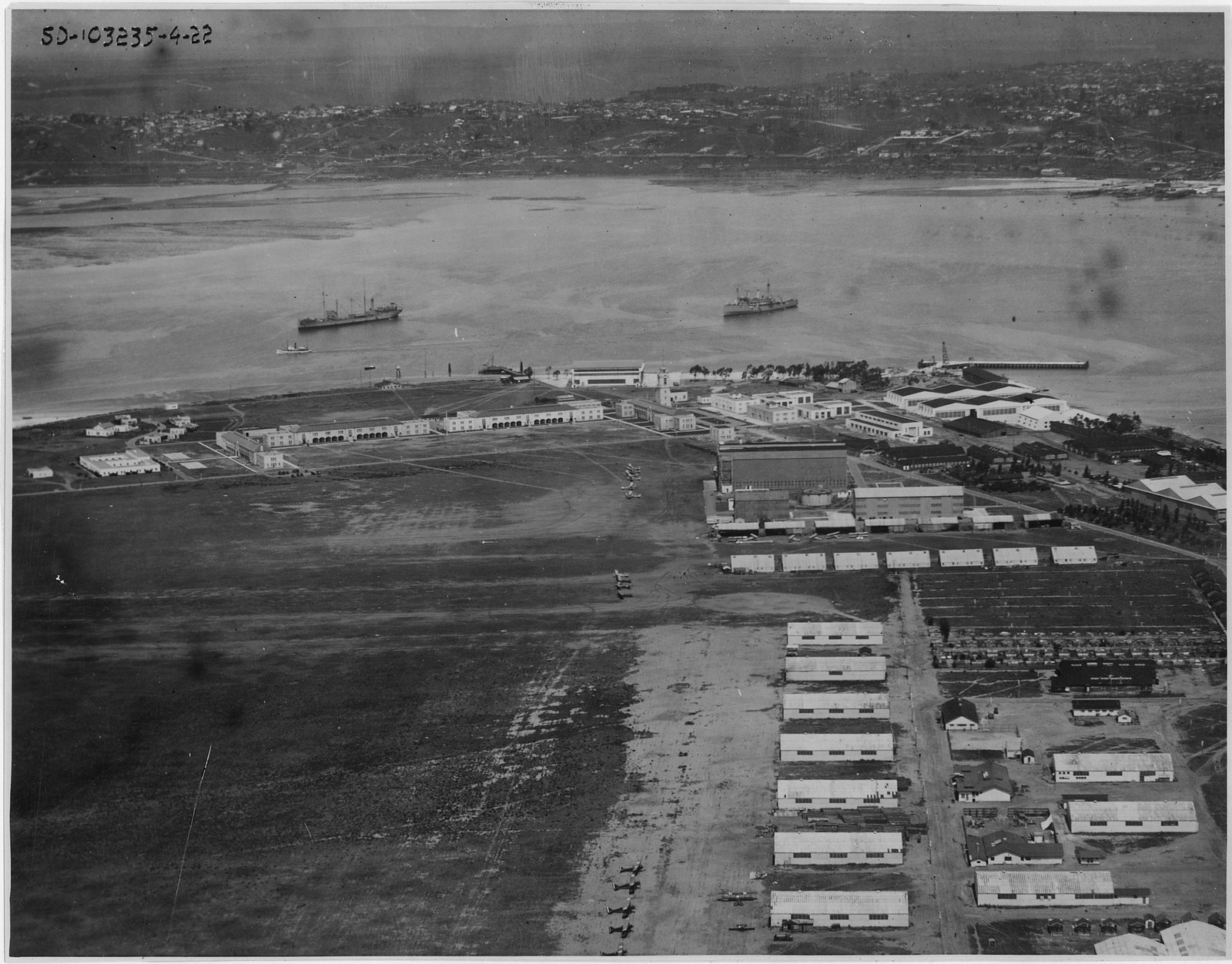 A low aerial photograph of the naval air station on North Island in May 1922, showing rows of hangars and barracks on flat open ground with ships at anchor in San Diego Bay beyond