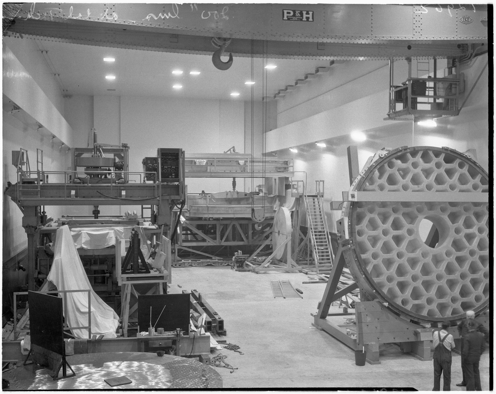 The 200-inch Pyrex telescope disk standing on edge in the Caltech optical shop in Pasadena in 1936, its back face cut into a deep honeycomb of ribs, with two men standing at its base for scale