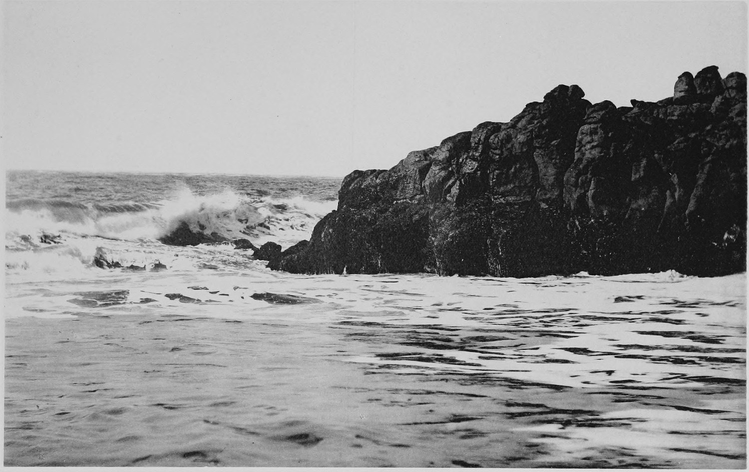 A long low rock reef running out into surf, waves breaking white along its near side