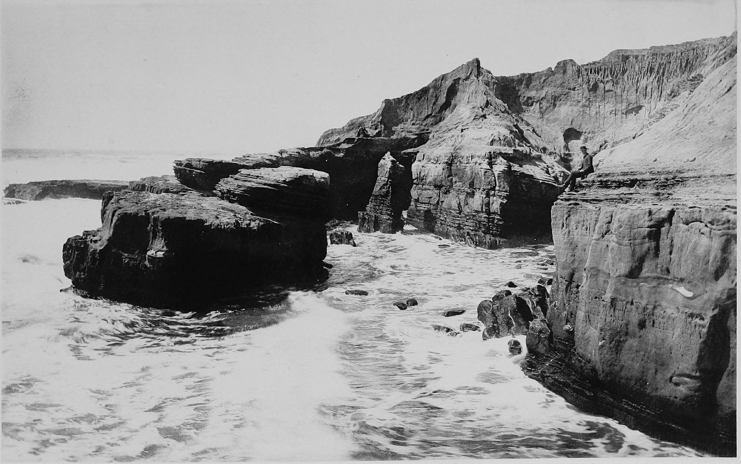 A sandstone point cut through by a natural arch, water pouring back off the rocks in the foreground