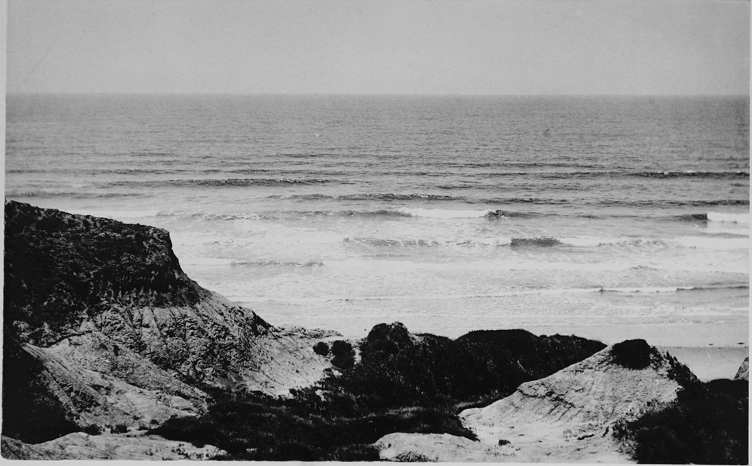 A low dark reef in the foreground with open ocean beyond and a long line of small surf