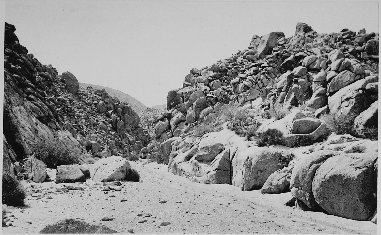 A sandy track running up between huge rounded granite boulders piled on both sides