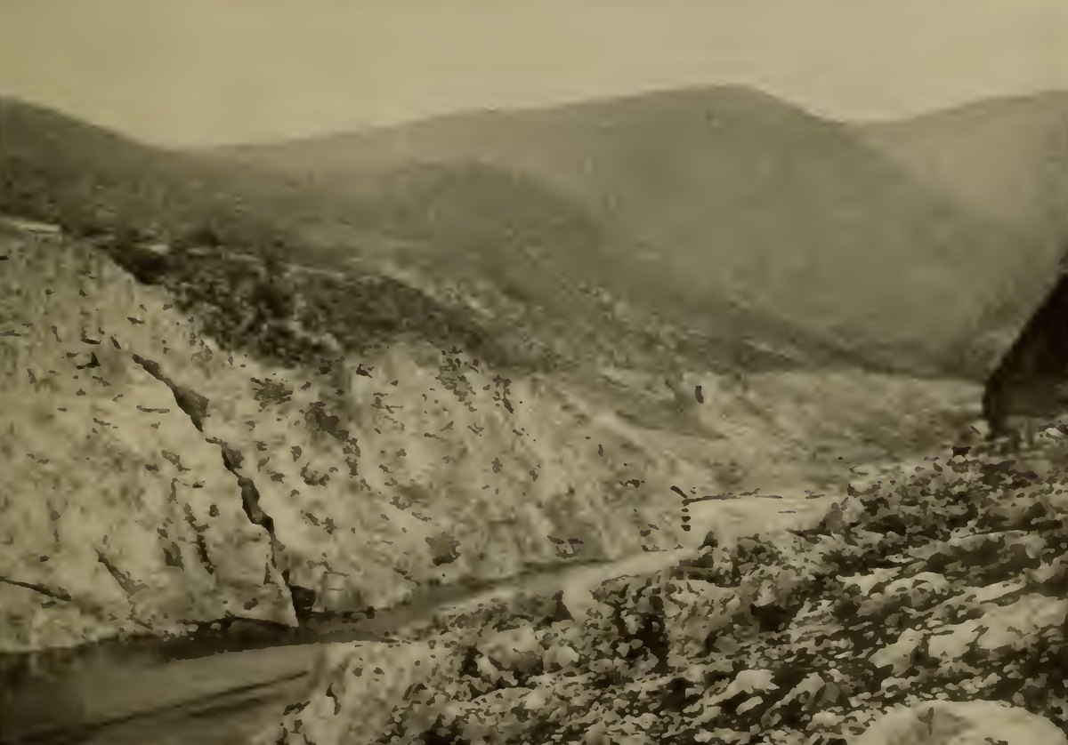 A rocky canyon with bare slopes and a thin stream running through the bottom where a dam once stood