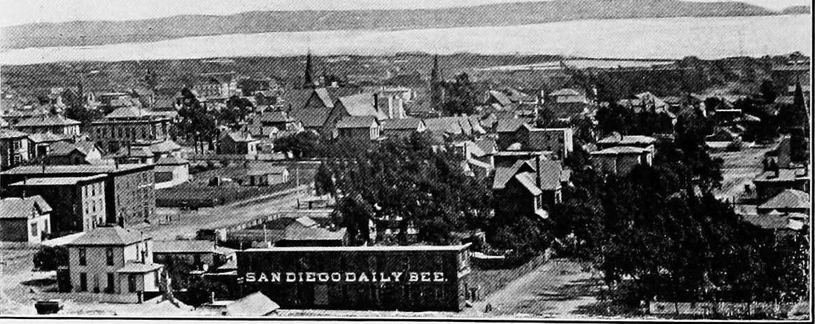 Rooftops of a busy town with church spires, a building marked San Diego Daily Bee, and the bay beyond
