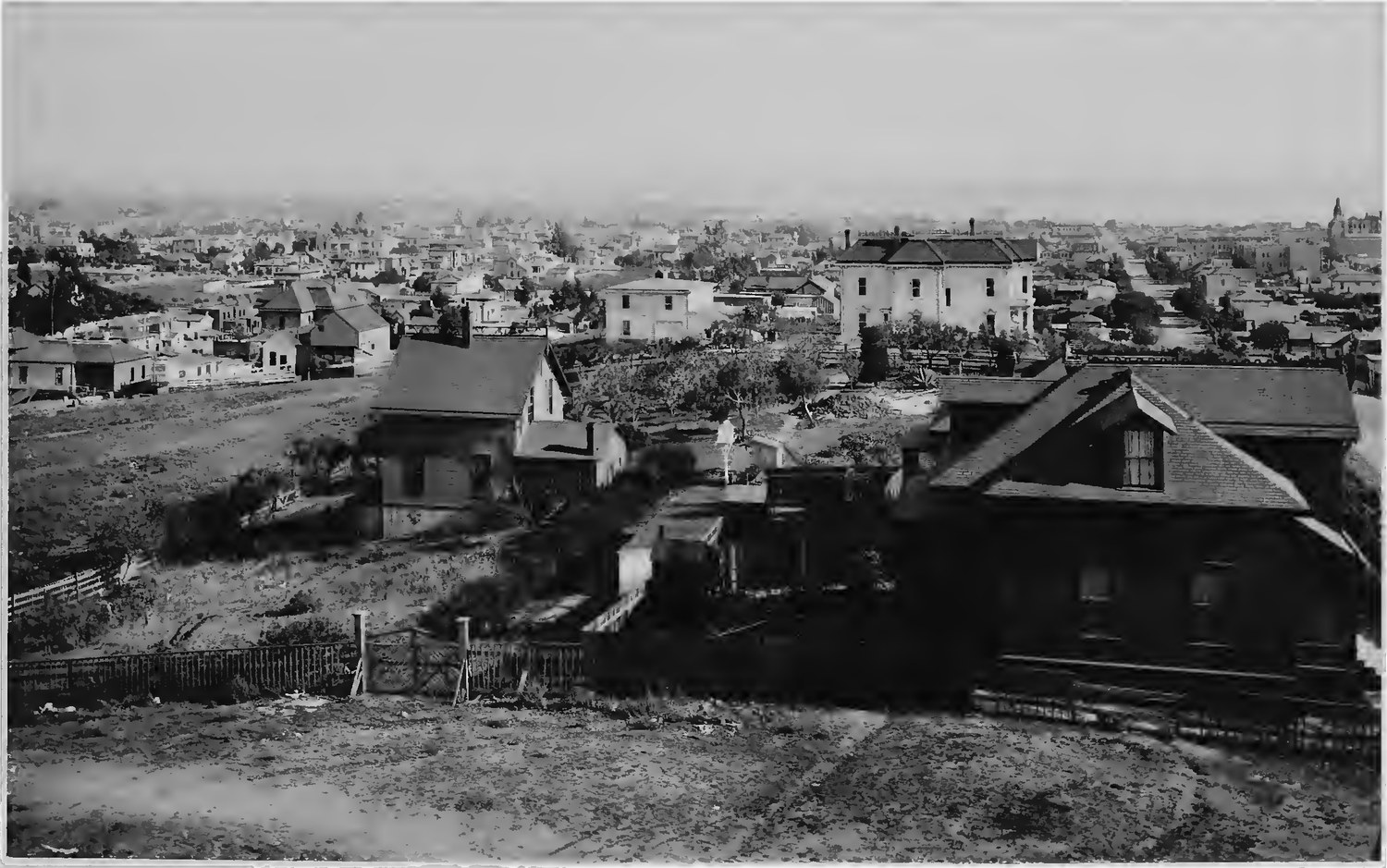 San Diego photographed in 1887 looking southeast from a rise, scattered wooden houses and open dirt lots in the foreground falling away to the built up town beyond