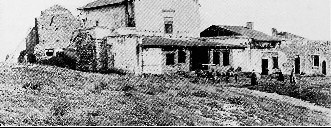 The roofless adobe walls and broken front of the old mission on a grassy slope