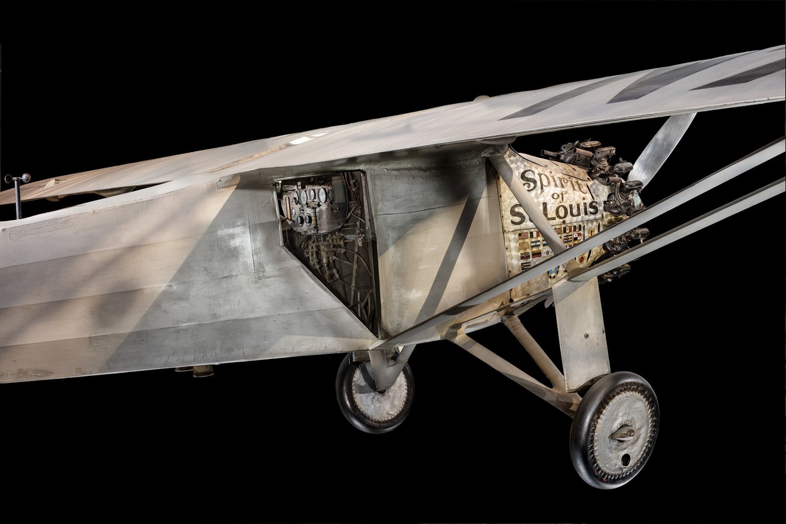 A silver single engine monoplane seen from below, its name painted on the nose