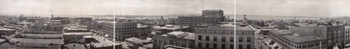 A long panoramic photograph across the rooftops of a low downtown of brick blocks toward the bay