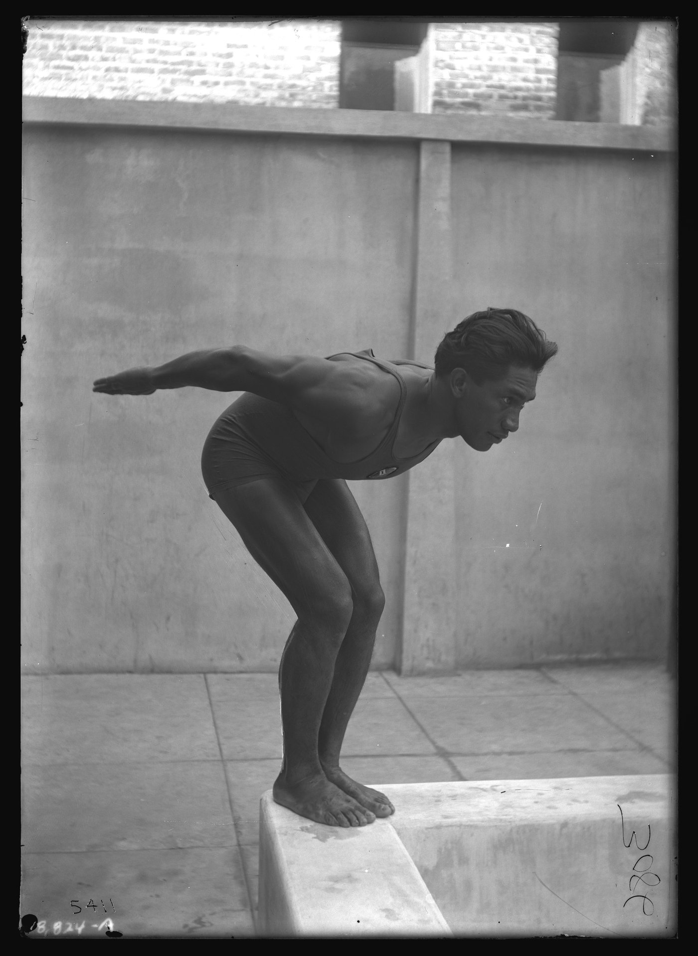 Duke Kahanamoku crouched on a starting block at the edge of a pool