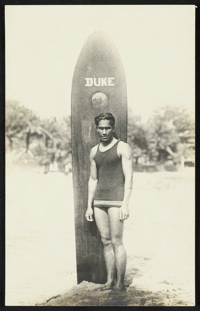 Duke Kahanamoku beside his own board, his name on the deck