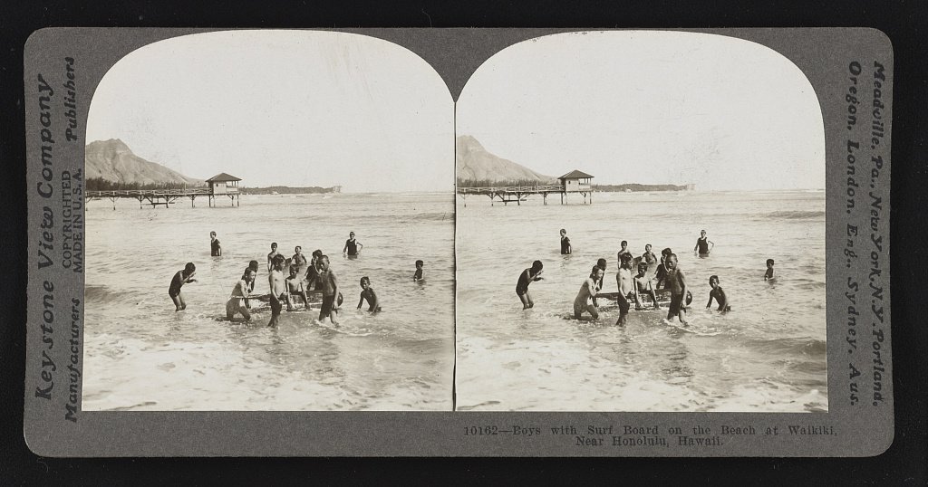 Boys with a surfboard on the beach at Waikiki