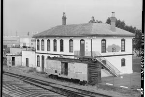 The two story wood National City railroad depot of 1882 seen from across the railroad tracks, with a boxcar standing against its west side
