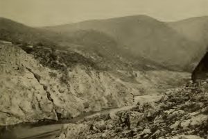 A rocky canyon with bare slopes and a thin stream running through the bottom where a dam once stood