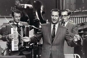Lawrence Welk conducting in front of his orchestra on a television stage, an accordion player at left
