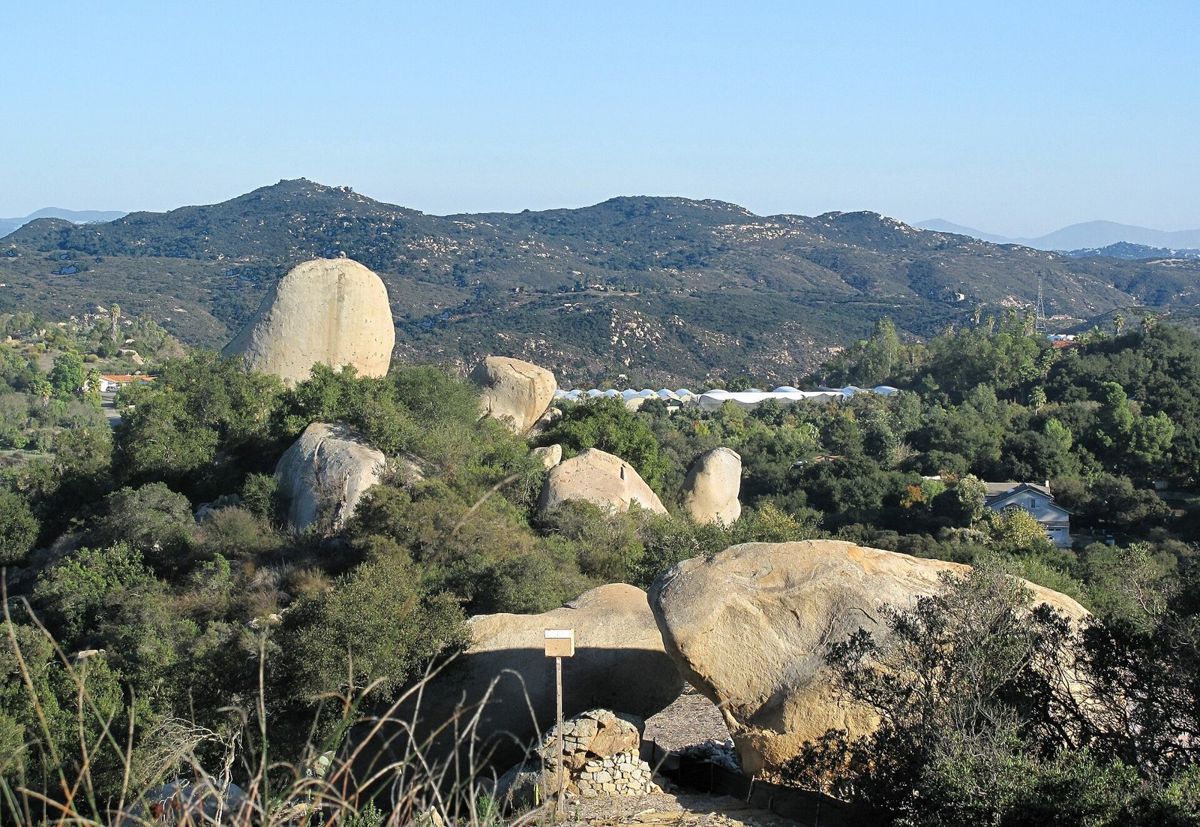 Huge rounded granite boulders among green chaparral, rolling hills and mountains behind under a clear sky