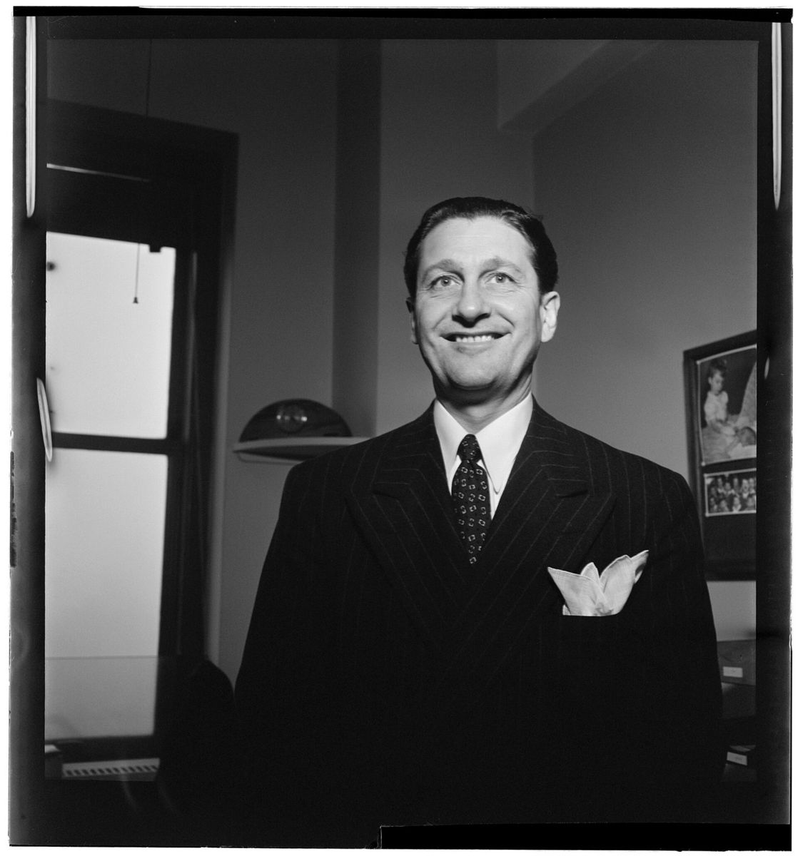 A smiling man in a pinstriped double breasted suit with a pocket square standing in an office